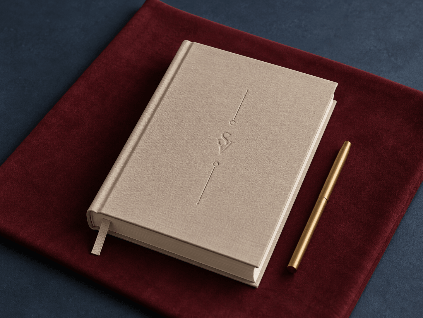 Zamknięty SVOYA Journal z monogramem i mosiężny długopis na bordowej aksamitnej tkaninie, pod spodem ciemny granat